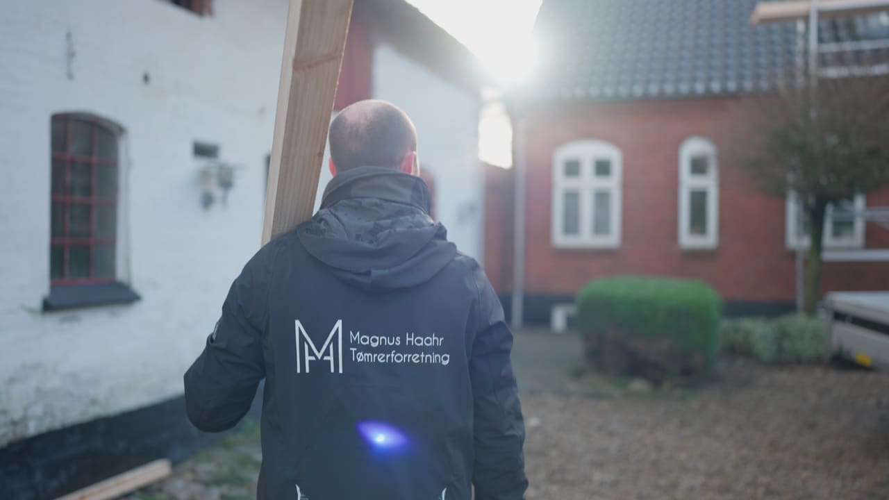 Tømrer i Magnus Haahr-jakke foran et rødstenshus