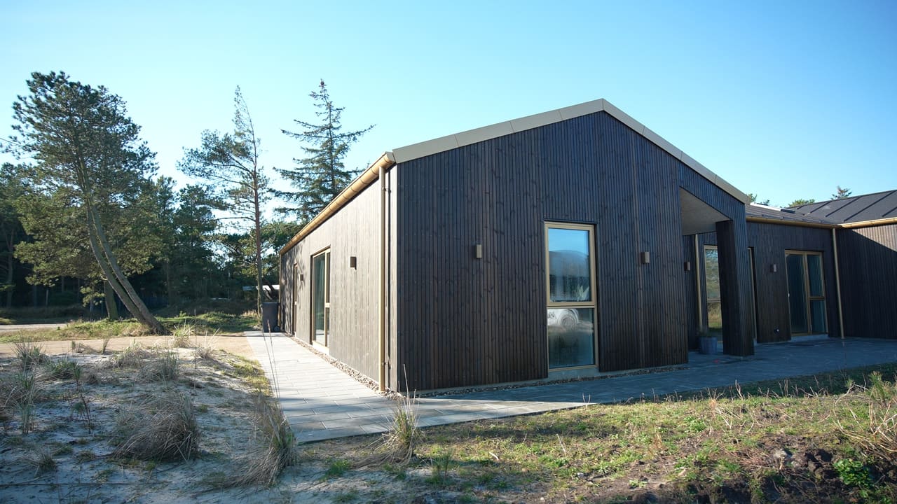 Sort træhus i klitlandskab